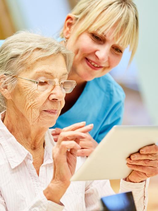 Pflegekraft hilft Seniorin mit Tablet-Computer Pflegekraft hilft Seniorin mit Tablet-Computer