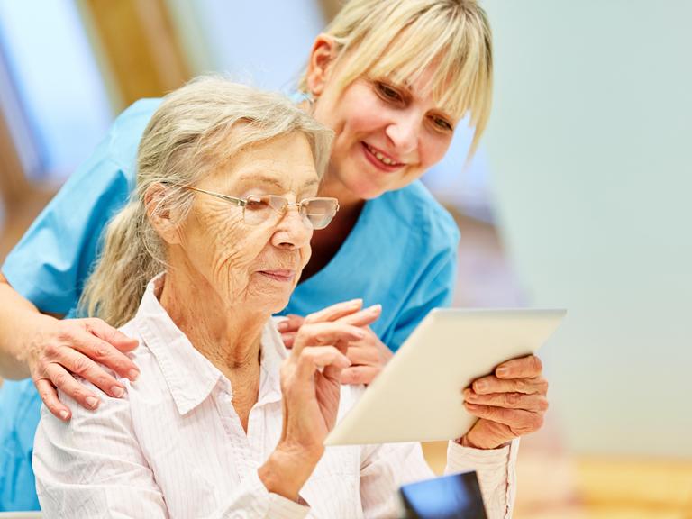 Pflegekraft hilft Seniorin mit Tablet-Computer Pflegekraft hilft Seniorin mit Tablet-Computer
