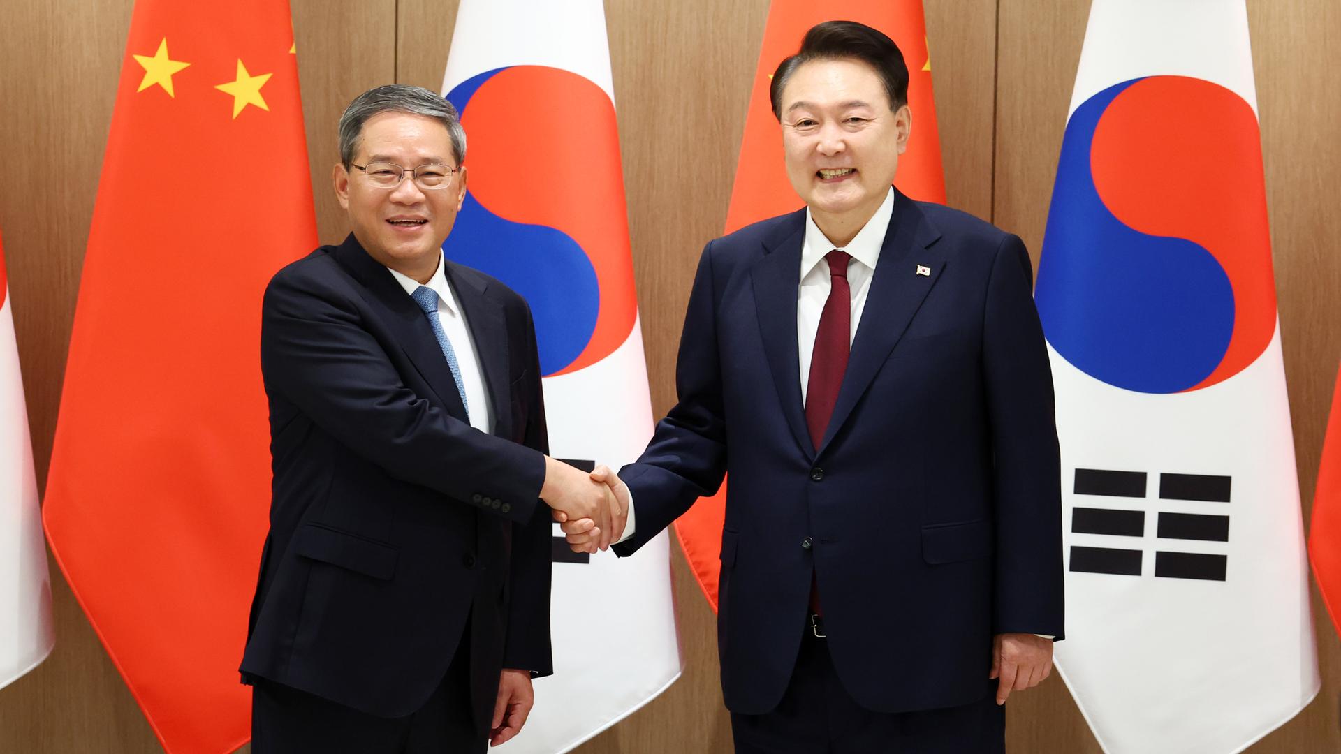 Der südkoreanische Präsident Yoon und der chinesische Ministerpräsident Li geben sich die Hand und lächeln in die Kamera. Der südkoreanische Präsident Yoon und der chinesische Ministerpräsident Li geben sich die Hand und lächeln in die Kamera.