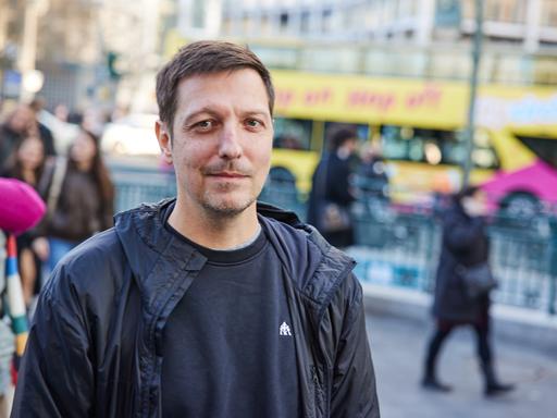 Der Autor, Journalist und Fernsehmoderator Thilo Mischke während eines Photocalls. Im Hintergrund ist unscharf eine viel befahrene Straße zu erkennen. Mischke schaut ernst. 