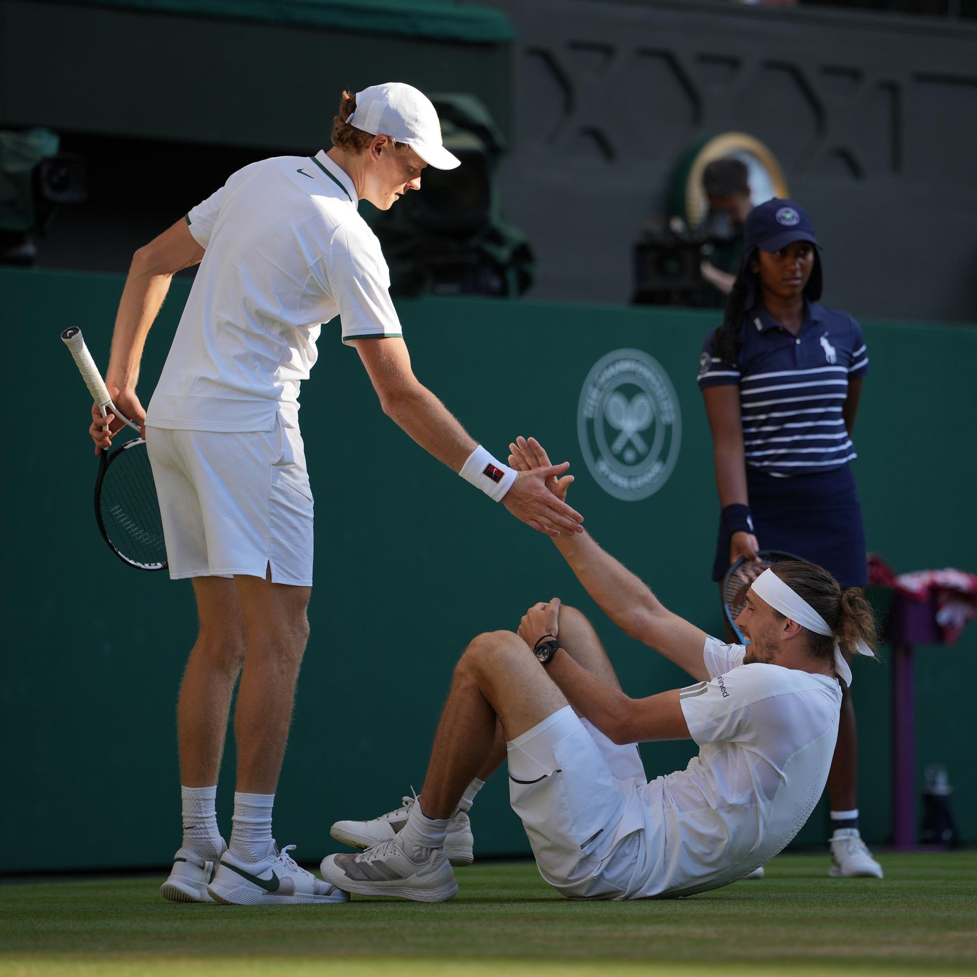 Tennis-Spieler Jannik Sinner hilft Alexander Zverev auf, der während des Wimbledon-Finales gestürzt war.