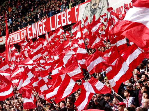 In der Fankurve von Fortuna Düsseldorf werden zahlreiche rot-weiße Fahnen geschwenkt.
