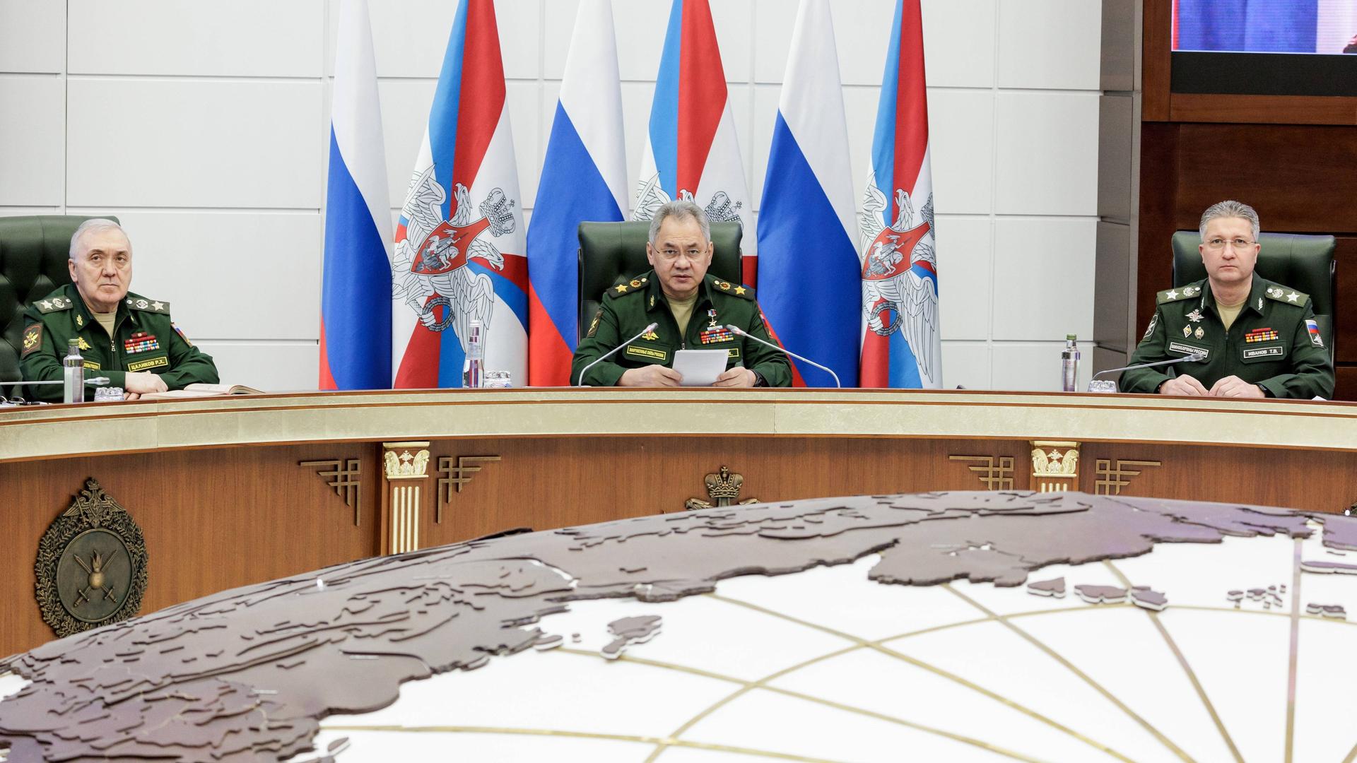 Der russische Verteidigungsminister Schoigu sitzt mit zwei Mitarbeitern an einem runden Tisch. Vor ihnen ein großer Tisch in Form der Erdkugel. Der russische Verteidigungsminister Schoigu sitzt mit zwei Mitarbeitern an einem runden Tisch. Vor ihnen ein großer Tisch in Form der Erdkugel.