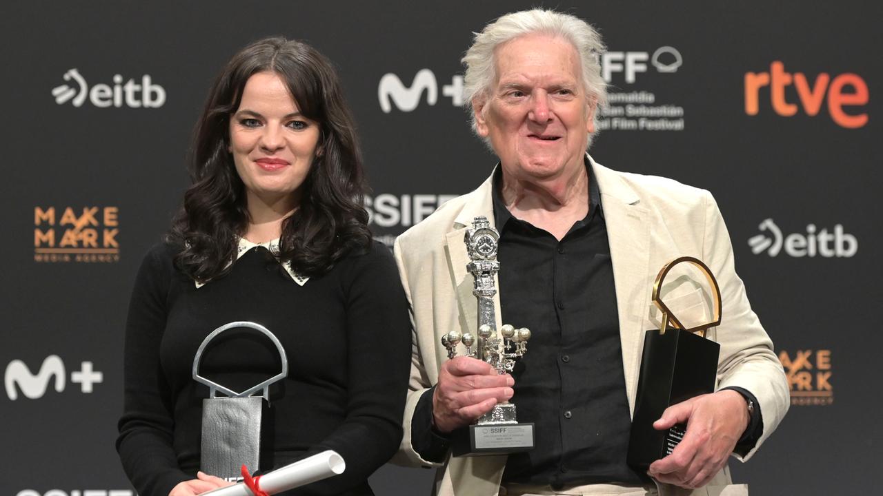 Die Schauspielerin Alice Bailey Johnson und der Schauspieler Paul Jesson halten beim Filmfefst in San Sebastian mehrere Preise in ihren Händen. Hinter ihnen eine Wand mit den Logos der Sponsoren.