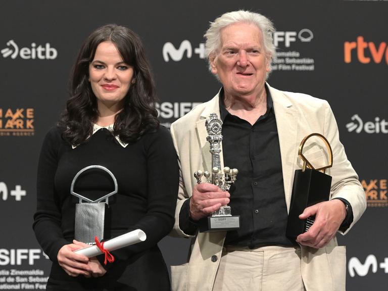 Die Schauspielerin Alice Bailey Johnson und der Schauspieler Paul Jesson halten beim Filmfefst in San Sebastian mehrere Preise in ihren Händen. Hinter ihnen eine Wand mit den Logos der Sponsoren. Die Schauspielerin Alice Bailey Johnson und der Schauspieler Paul Jesson halten beim Filmfefst in San Sebastian mehrere Preise in ihren Händen. Hinter ihnen eine Wand mit den Logos der Sponsoren.