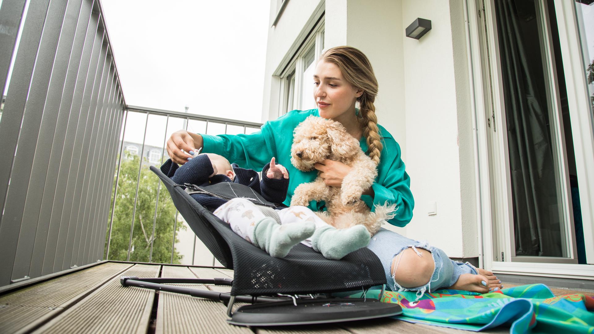Eine Frau kümmert sich auf dem heimischen Balkon um ihr Kind und den Hund.