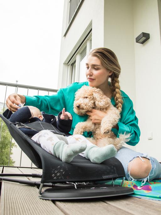 Eine Frau kümmert sich auf dem heimischen Balkon um ihr Kind und den Hund.