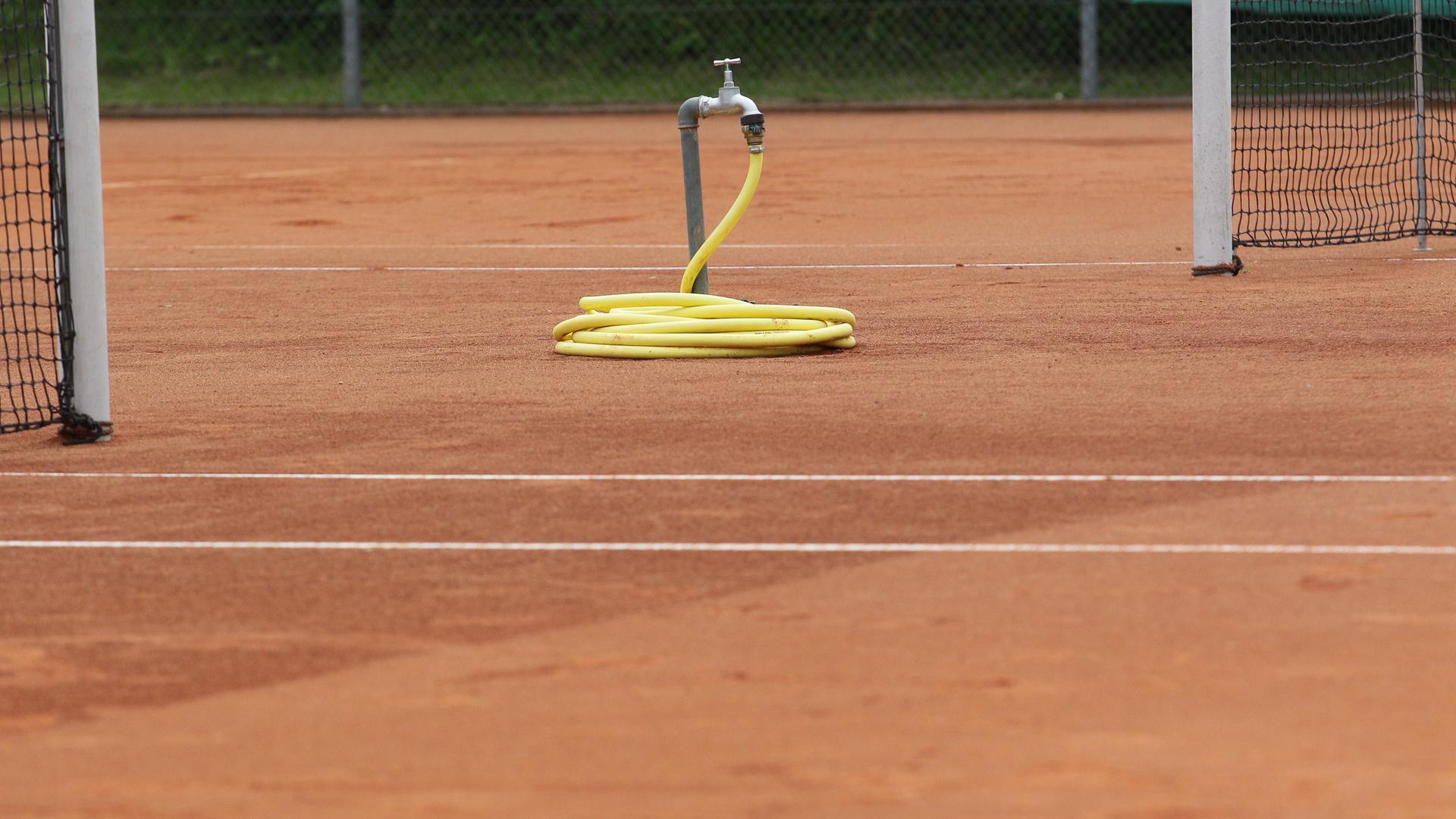 Ein Wasseranschluss mit zusammengerolltem Schlauch auf einem Tennisplatz Ein Wasseranschluss mit zusammengerolltem Schlauch auf einem Tennisplatz