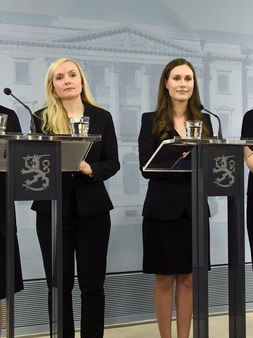 Vier Frauen und ein Mann stehen bei einer Pressekonferenz an Mikrofonen.