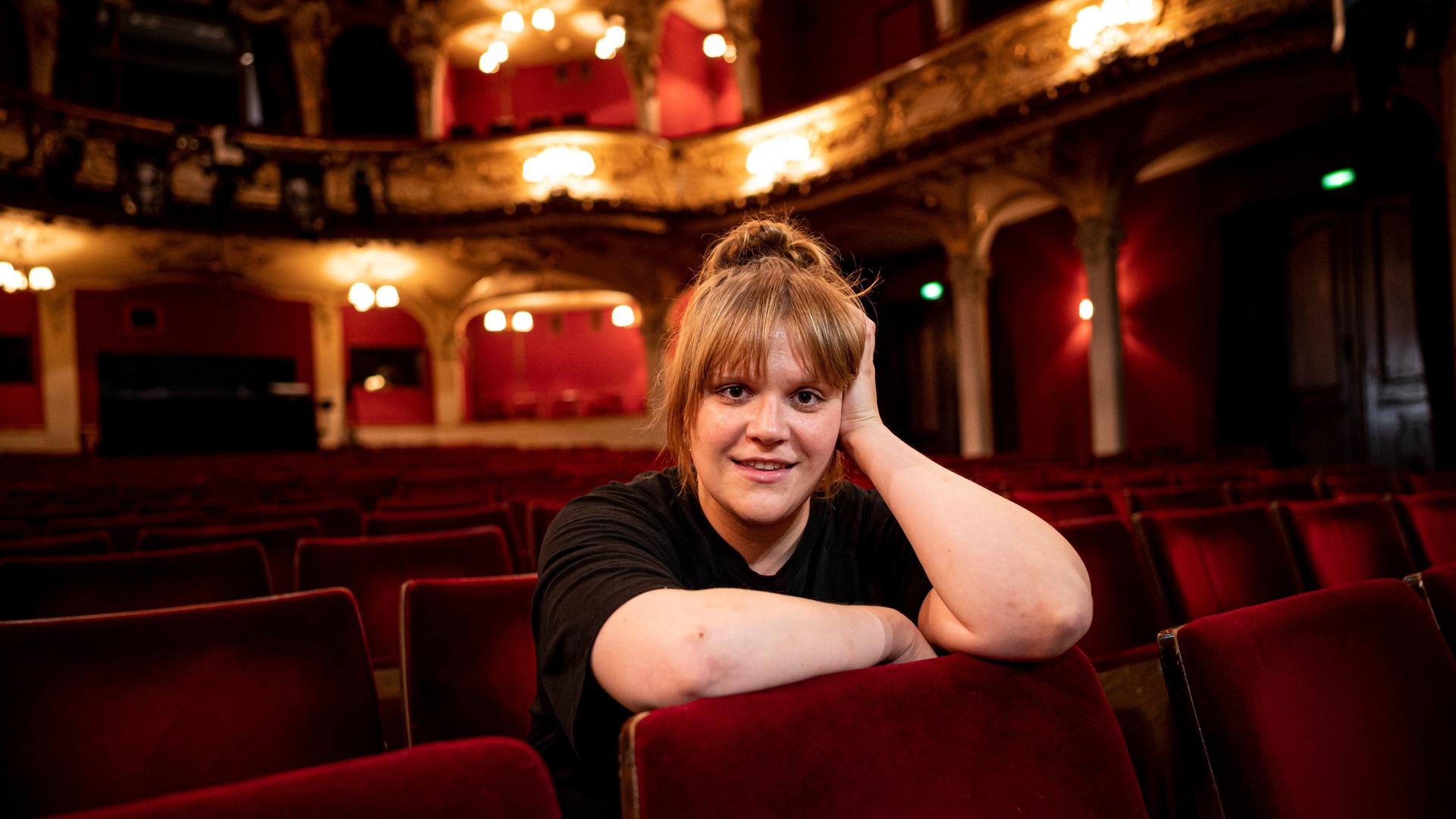 Stefanie Reinsperger sitzt im Zuschauerraum des Berliner Ensembles. Sie trägt ein schwarzes T-Shirt und das rotblonde Haar zum Dutt aufgesteckt.
