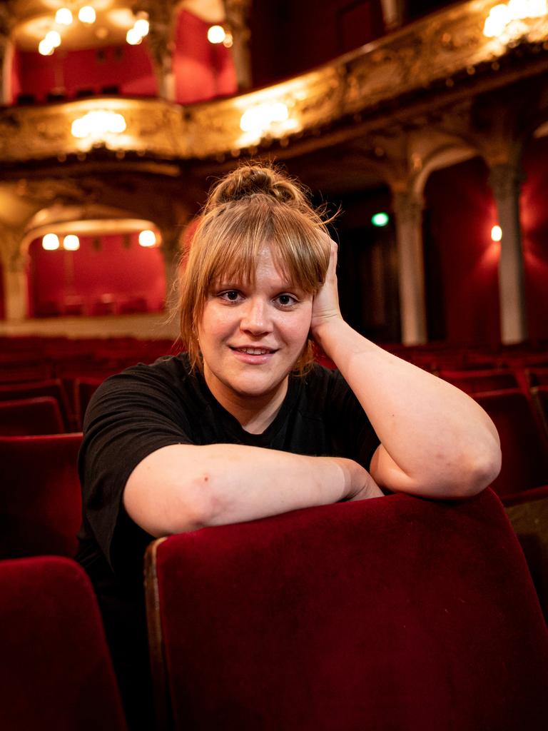 Stefanie Reinsperger sitzt im Zuschauerraum des Berliner Ensembles. Sie trägt ein schwarzes T-Shirt und das rotblonde Haar zum Dutt aufgesteckt.