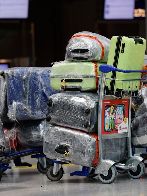 Reisekoffer stehen am Düsseldorfer Flughafen auf einem Trolley vor dem Check-In-Schalter. Die Koffer sind mit Folie geschützt.