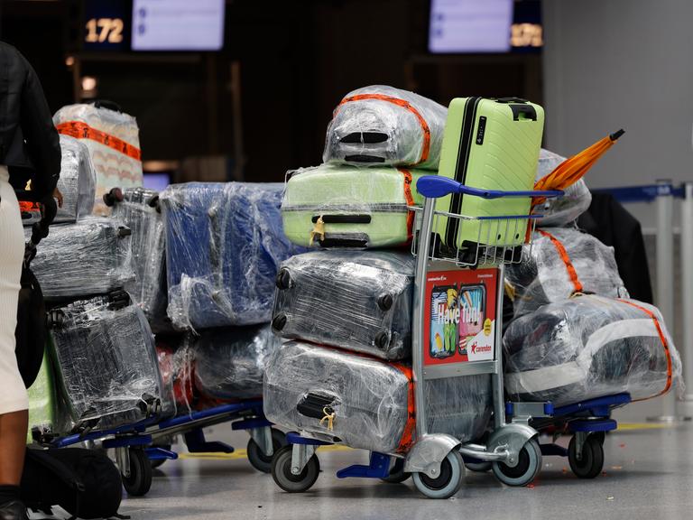 Reisekoffer stehen am Düsseldorfer Flughafen auf einem Trolley vor dem Check-In-Schalter. Die Koffer sind mit Folie geschützt.