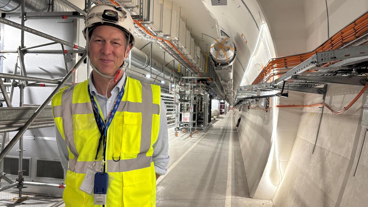 Markus Zerlauth, Projektleiter HL-LHC, steht mit Warnweste und Helm bekleidet in einem neuen Servicetunnel aus Beton mit Kabeln und Rohren.
