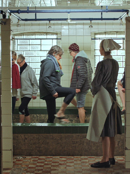 Eine Gruppe von Menschen beim "Wassertreten" im ehemaligen Kinderkurheim Johannaberg bei Detmold. Im Vordergrund eine Frau, die eine Schwesteruiform aus vergangenen Zeiten trägt

