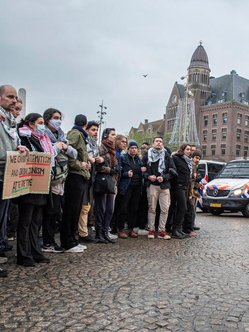 Eine große Gruppe von Demonstranten steht umgeben von niederländischen Polizeifahrzeugen. 