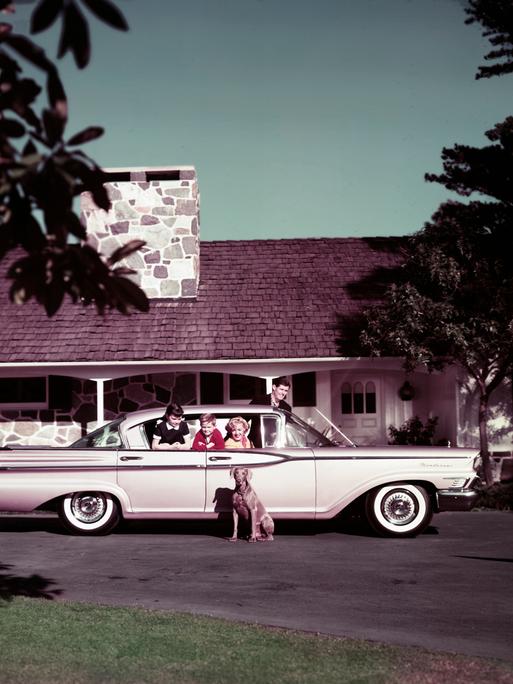 Eine vierköpfige Familie in ihrem Mercury Monterey-Auto auf der Einfahrt ihres Hauses, 1959. Ihr Hund sitzt neben dem Auto.