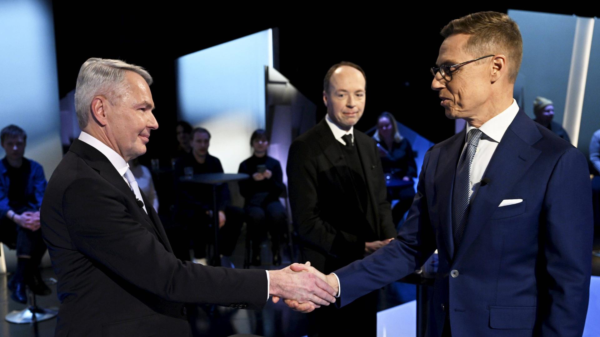 Zwei Männer geben sich die Hand während einer Gesprächsrunde mit Publikum.