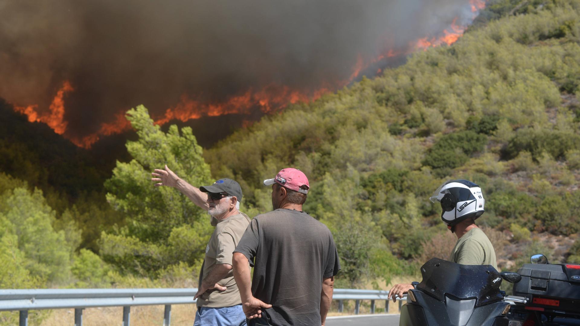 Griechenland, Varnavas, der Norden Athens. Dort beobachten Passanten einen Waldbrand. Aufnahme vom 12. August 2024