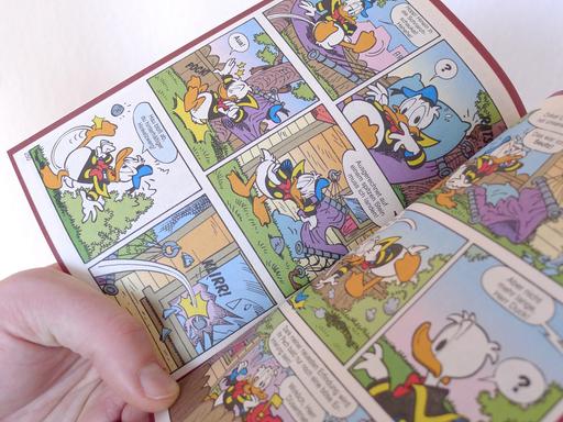 Eine Hand hält ein offenes Donald Duck Heft, ein LTB, "Lustiges Taschenbuch Comic".