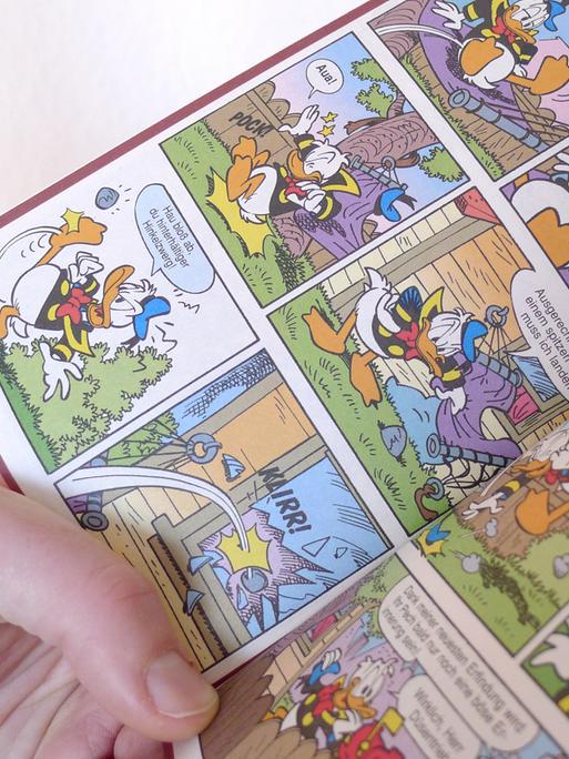 Eine Hand hält ein offenes Donald Duck Heft, ein LTB, "Lustiges Taschenbuch Comic".