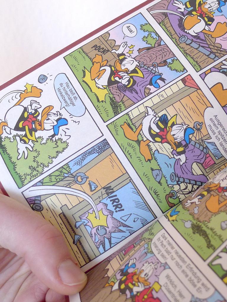 Eine Hand hält ein offenes Donald Duck Heft, ein LTB, "Lustiges Taschenbuch Comic".