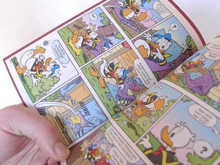 Eine Hand hält ein offenes Donald Duck Heft, ein LTB, "Lustiges Taschenbuch Comic".