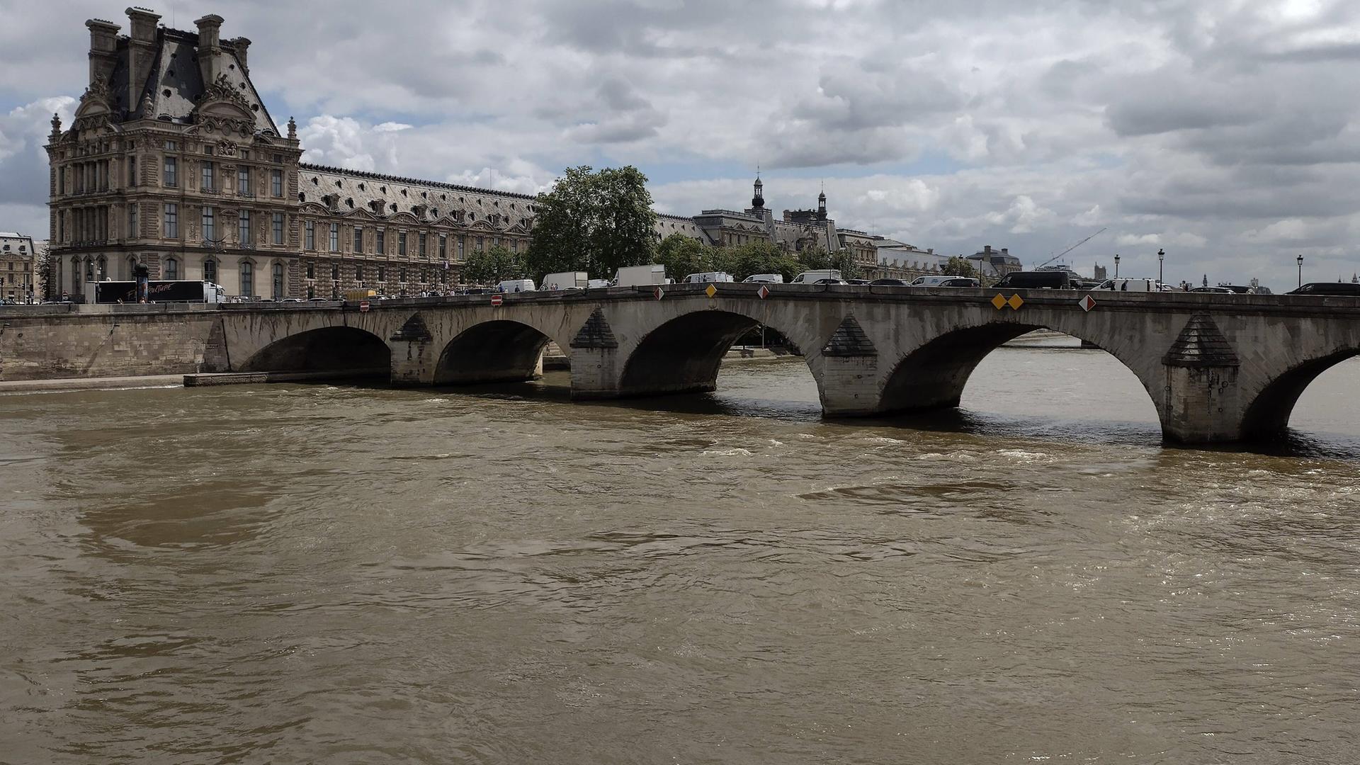 Zu sehen ist die Seine mit einer Brücke, im Hintergrund der Louvre.