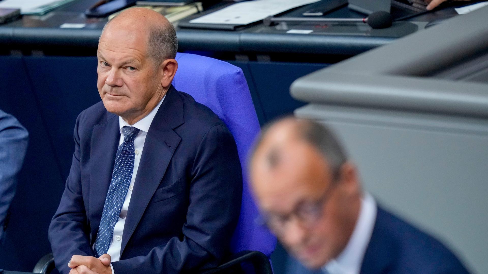 Olaf Scholz betrachtet Friedrich Merz am Rednerpult.