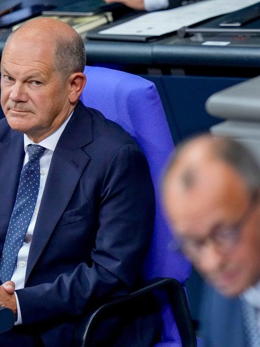 Olaf Scholz betrachtet Friedrich Merz am Rednerpult.