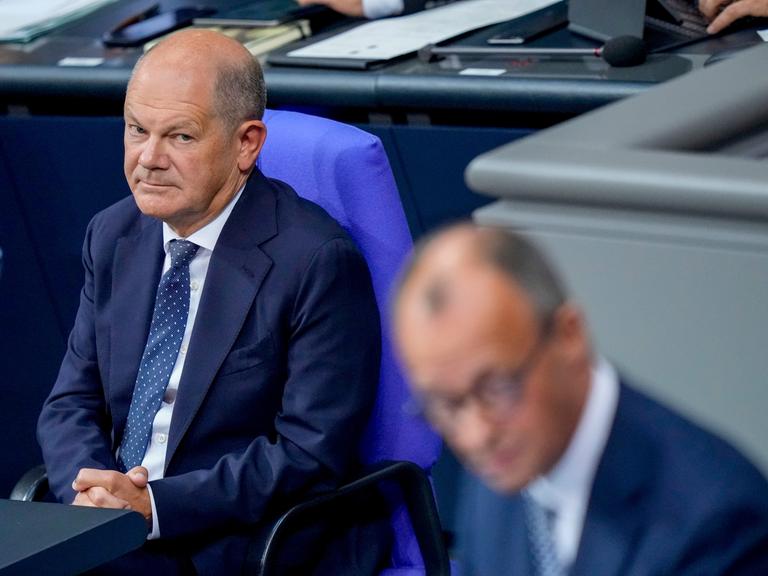 Olaf Scholz betrachtet Friedrich Merz am Rednerpult.