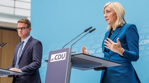 Bundesgesundheitsministerin Warken (r.) und CDU-Generalsekretär Linnemann bei einer CDU-Veranstaltung im vergangenen Jahr. Sie stehen jeweils an einem Rednerpult mit dem CDU-Logo. Warken spricht in ein Mikrofon.