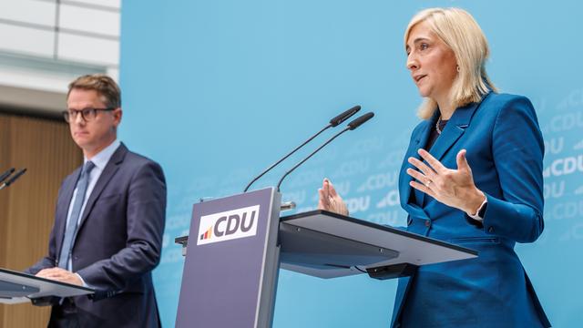 Bundesgesundheitsministerin Warken (r.) und CDU-Generalsekretär Linnemann bei einer CDU-Veranstaltung im vergangenen Jahr. Sie stehen jeweils an einem Rednerpult mit dem CDU-Logo. Warken spricht in ein Mikrofon.