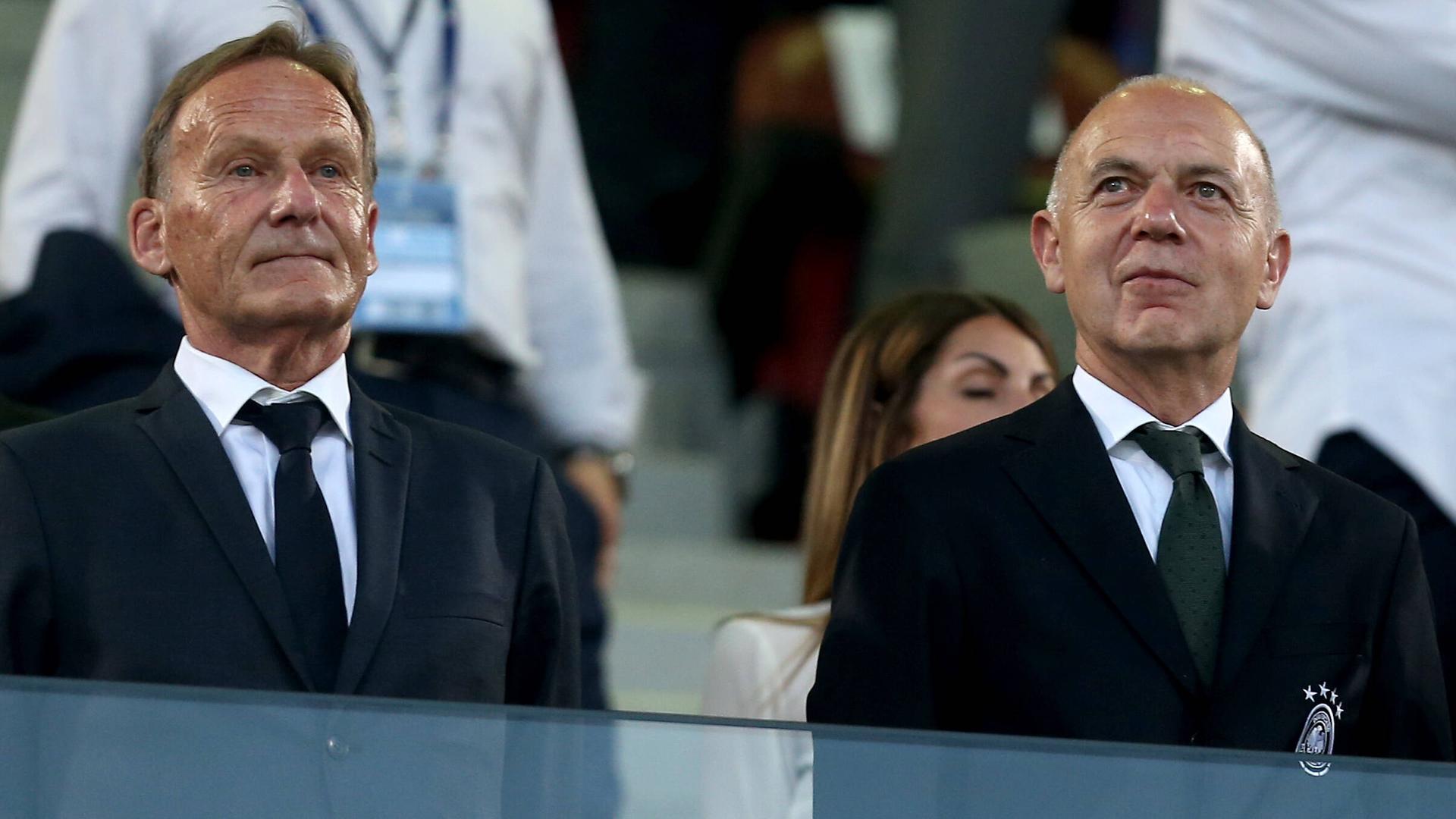 DFL-Aufsichtsratschef Hans-Joachim Watzke (l.) und DFB-Präsident Bernd Neuendorf stehen in schwarzen Anzügen auf einer Fußballtribüne nebeneinander. DFL-Aufsichtsratschef Hans-Joachim Watzke (l.) und DFB-Präsident Bernd Neuendorf stehen in schwarzen Anzügen auf einer Fußballtribüne nebeneinander.