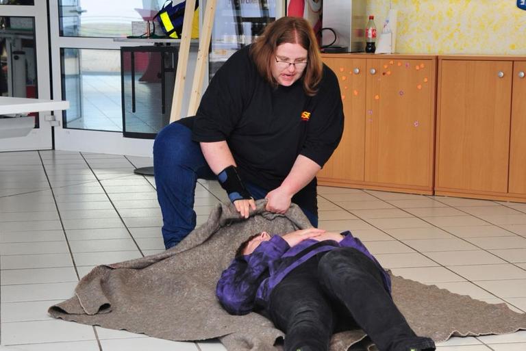 Während einer Übung zieht eine Fraue eine Person, die auf einer Decke liegt.