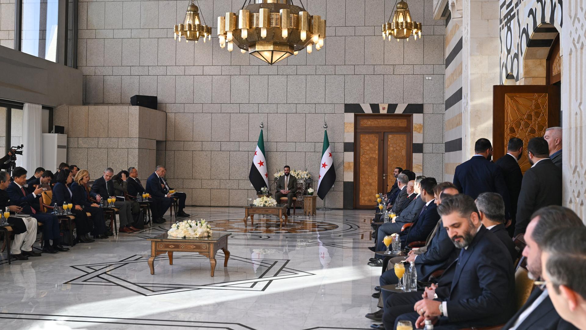 Der syrische Übergangspräsident Sharaa sitzt in der Mitte hinten in einem großen Raum, rechts davon die Delegation des Sicherheitsrates, links von ihm Mitglieder seiner Regierung.