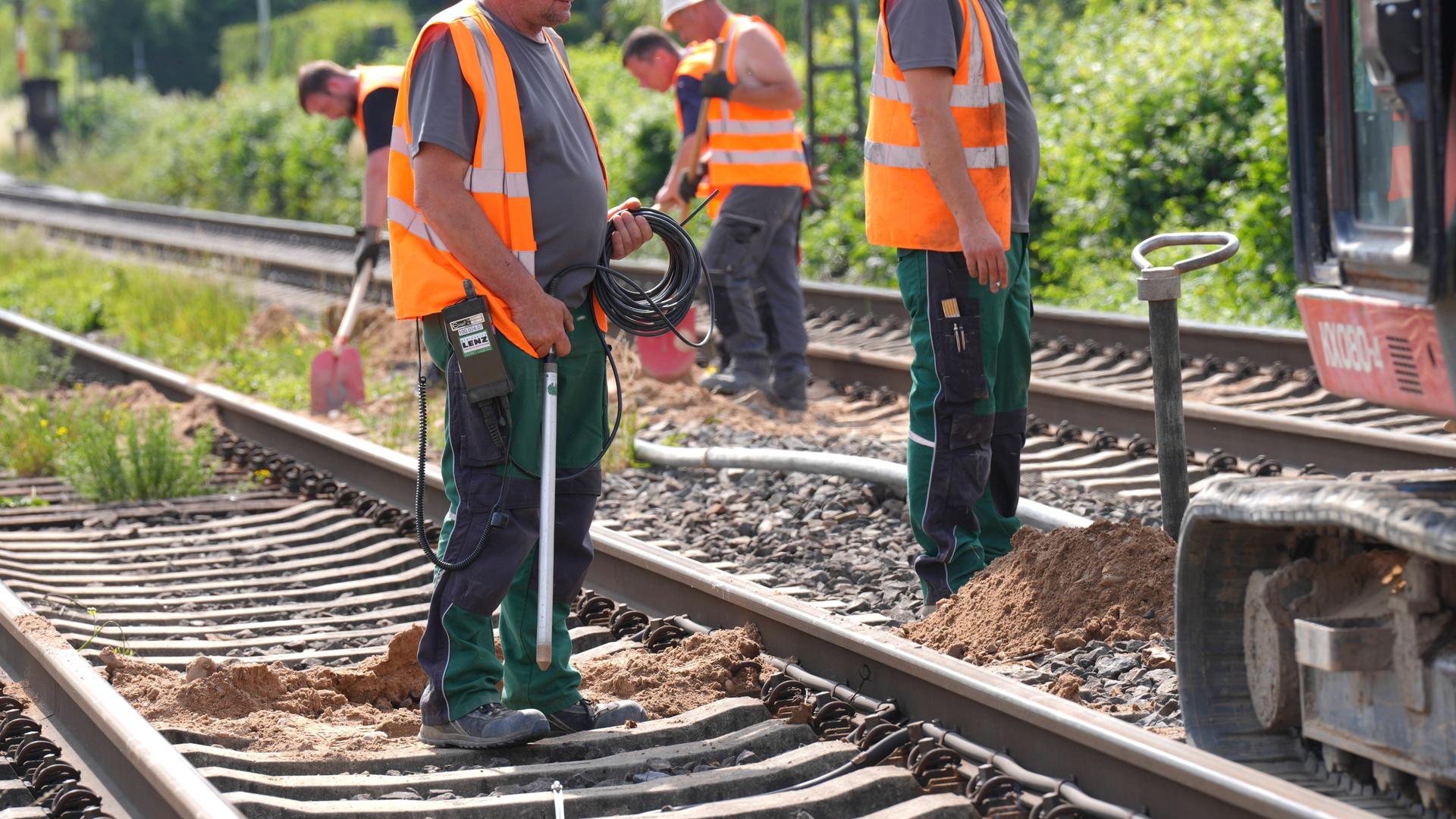 Arbeiter in orangen Warnwesten führen Gleisbauarbeiten durch.