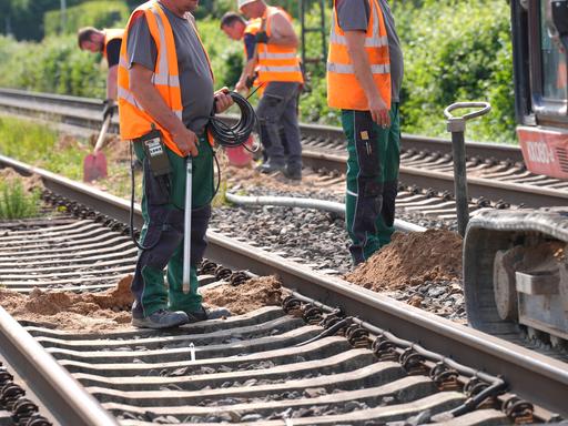 Arbeiter in orangen Warnwesten führen Gleisbauarbeiten durch.