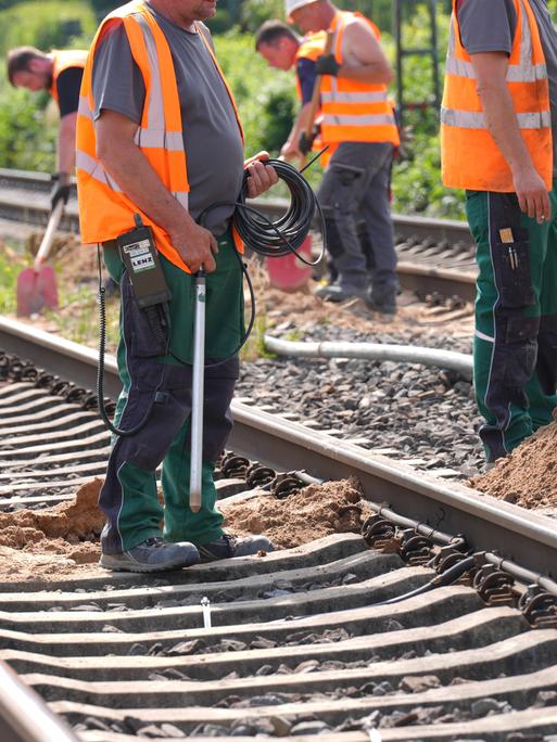 Arbeiter in orangen Warnwesten führen Gleisbauarbeiten durch.