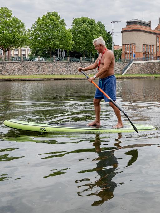 Ein weißhaariger Mann paddelt im Stehen auf einem SUP-Board auf der Elbe im Zentrum von Hradec Králové in der Tschechischen Republik