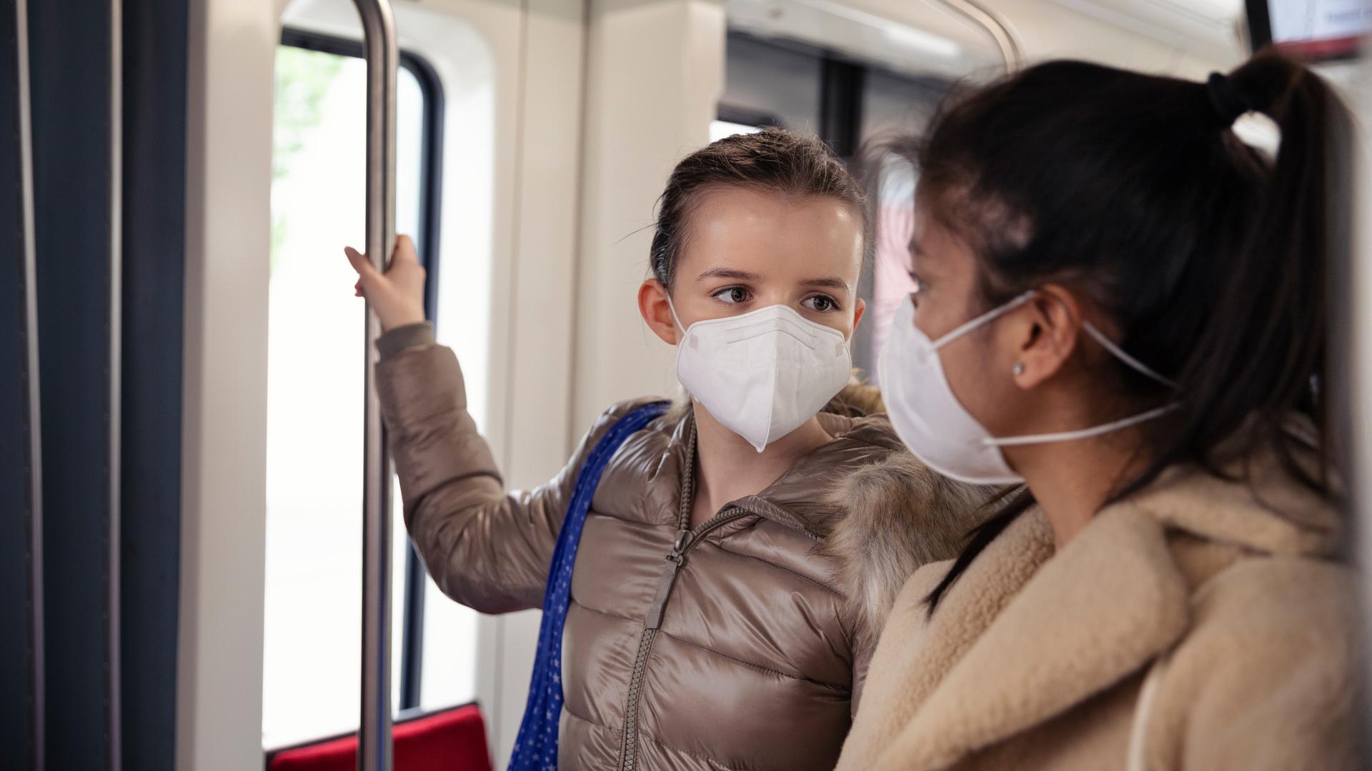 Zwei Teenager Mädchen tragen FFP2 Masken in einer U-Bahn.