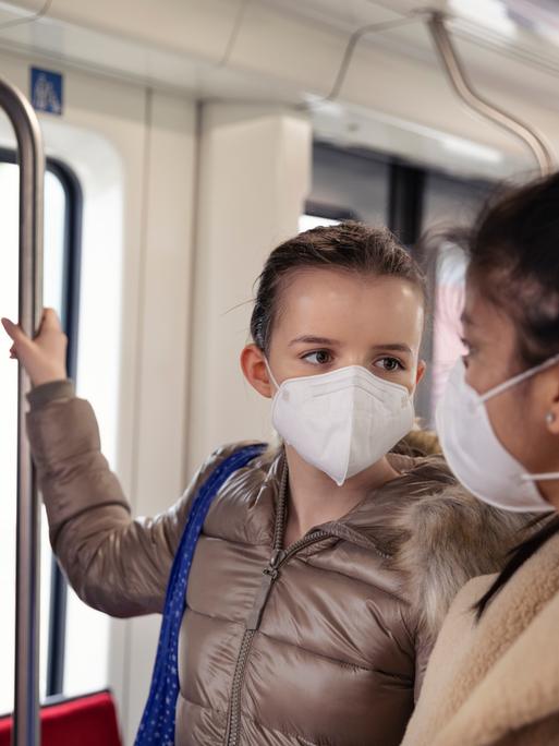 Zwei Teenager Mädchen tragen FFP2 Masken in einer U-Bahn.