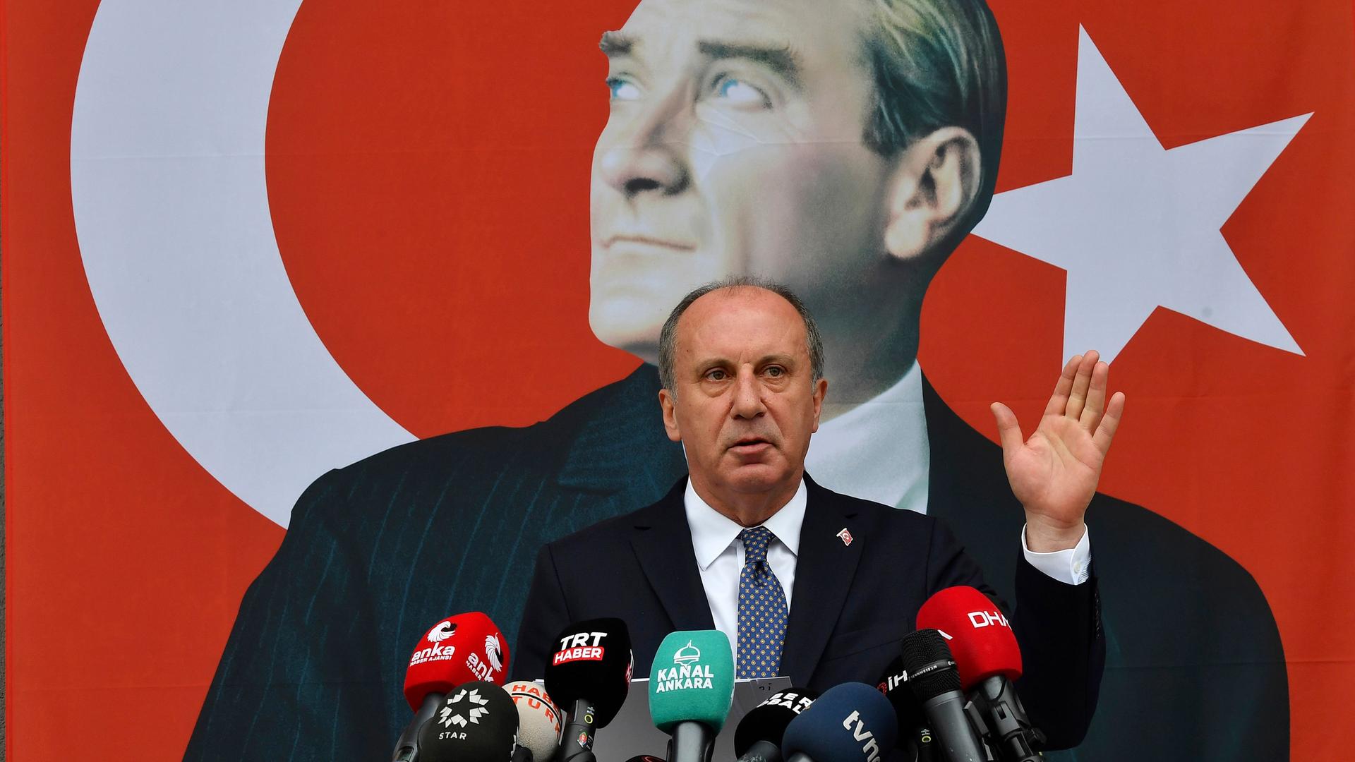 Ince steht an einem Redepult mit vielen Mikrofonen. Im Hintergrund ist ein Plakat, dass den Gründer der modernen Türkei, Atatürk, zeigt.