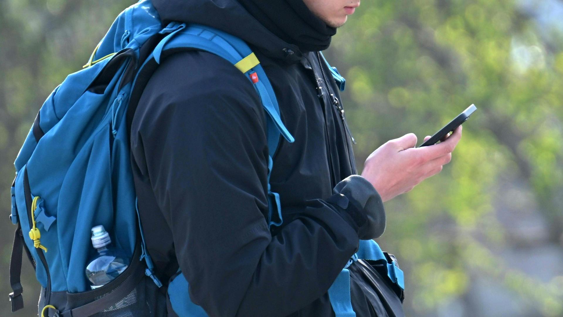 Ein Jugendlicher blickt auf ein Smartphone und trägt einen Schulranzen.