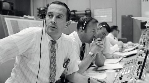 Männer mit Headsets sitzen vor alt anmutenden Tastaturen und Bildschirmen (Schwarz-Weiß-Foto)