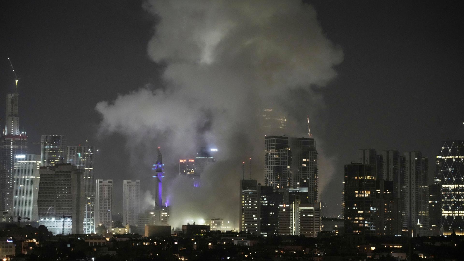 Es ist Nacht. Man sieht Gebäude und die Lichter von der Stadt Tel Aviv in Israel aus der Ferne. Dichter grauer Rauch steigt über Häusern auf. Es ist Nacht. Man sieht Gebäude und die Lichter von der Stadt Tel Aviv in Israel aus der Ferne. Dichter grauer Rauch steigt über Häusern auf.