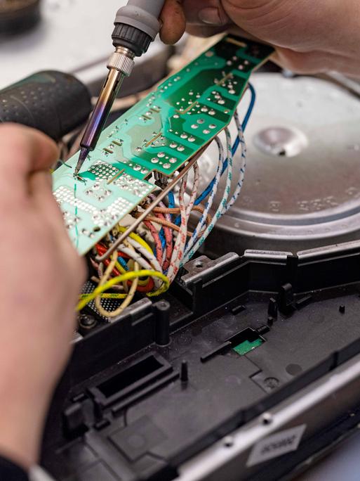 Reparatur-Cafe in Zella-Mehlis, Thueringen. Zwei Hände löten etwas an einer elektrischen Platine. Bislang werden nur relativ wenige Bauteile aus Elektrogeräten recycelt. 