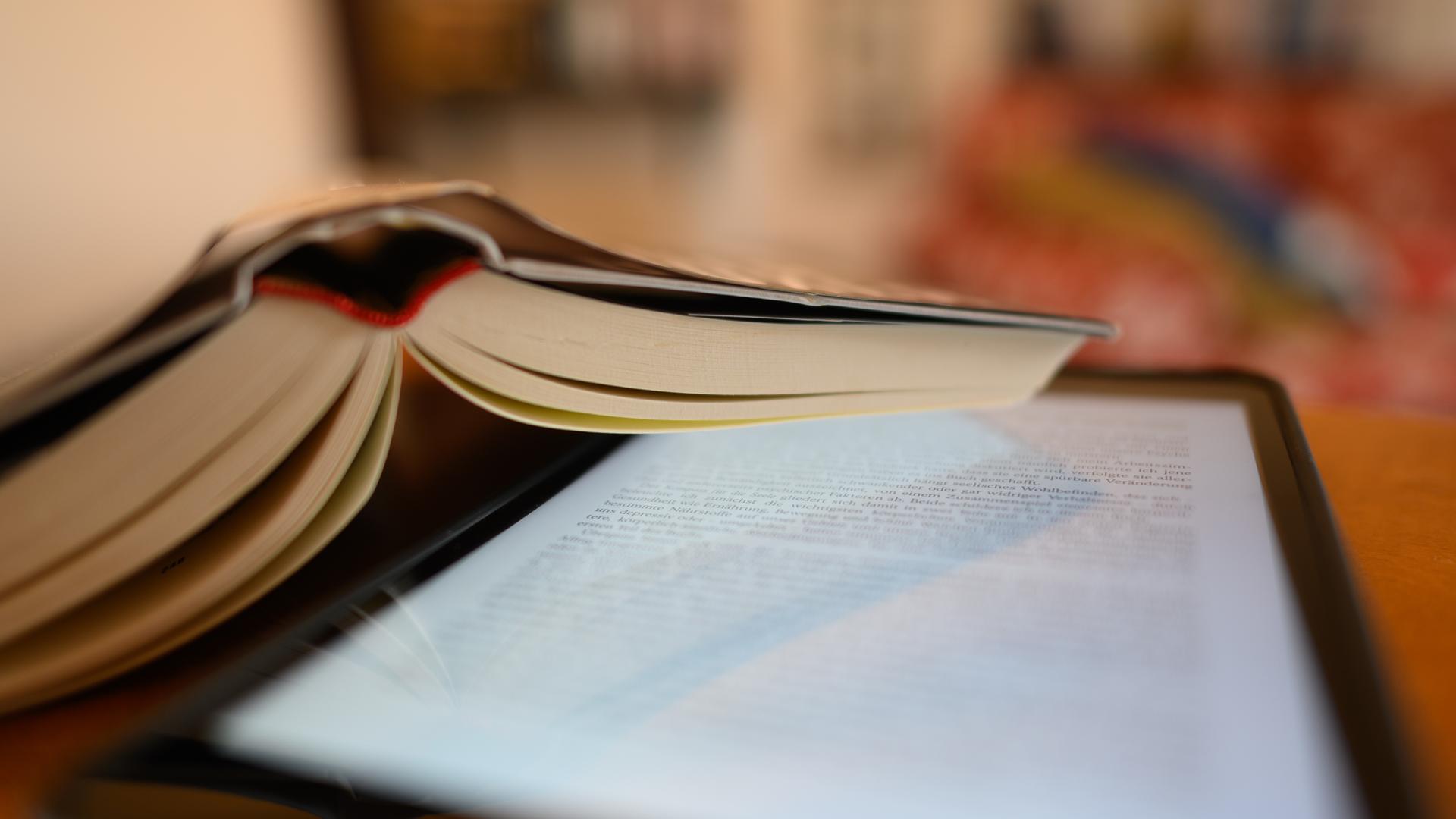 Ein Tablet und ein Buch liegen auf einem Tisch. Ein Tablet und ein Buch liegen auf einem Tisch.