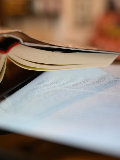 Ein Tablet und ein Buch liegen auf einem Tisch. Ein Tablet und ein Buch liegen auf einem Tisch.