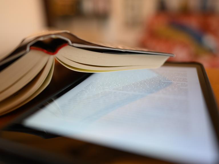 Ein Tablet und ein Buch liegen auf einem Tisch. Ein Tablet und ein Buch liegen auf einem Tisch.